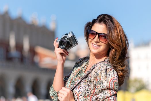 Beautiful and attractive woman holding a retro SLR camera and smiling on blurred background of a historic city