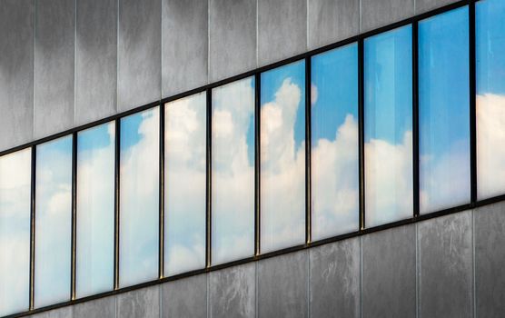 reflection of blue sky and white clouds in the windows of a gray building