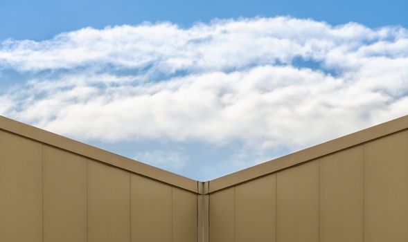 corner of a modern beige building and blue sky with white clouds