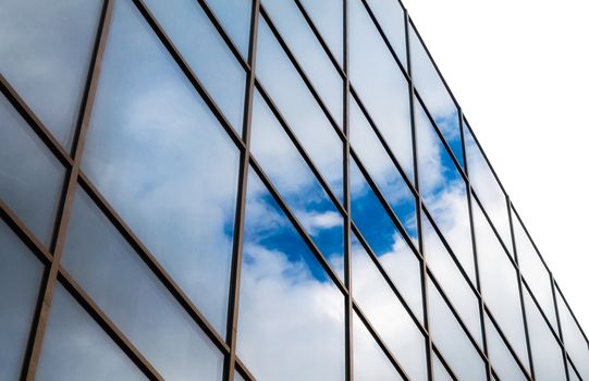 reflection of blue sky with white clouds in a window of a tall office building abstract architectural background