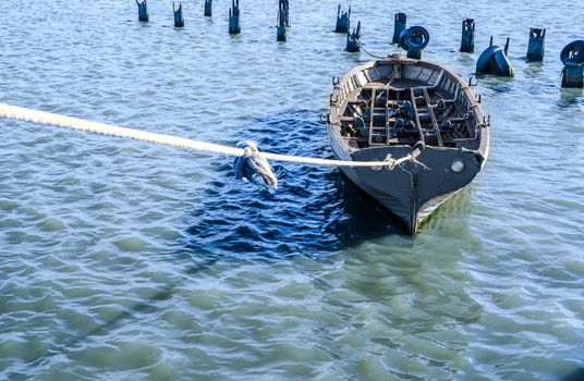 gray old fishing boat tied with a rope in blue-green water