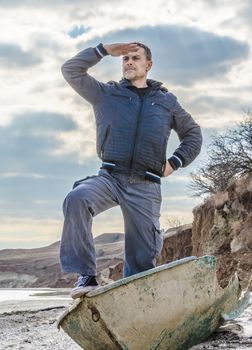 man in black stands in a broken boat on the beach and carefully looks into the distance