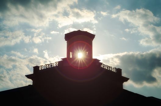 silhouette of an old building with sunbeams in the window against the sunset sky