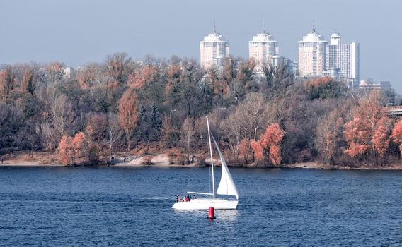 yacht with a white sail and tourists on the background of the coast and the city of Kiev Ukraine in the autumn morning