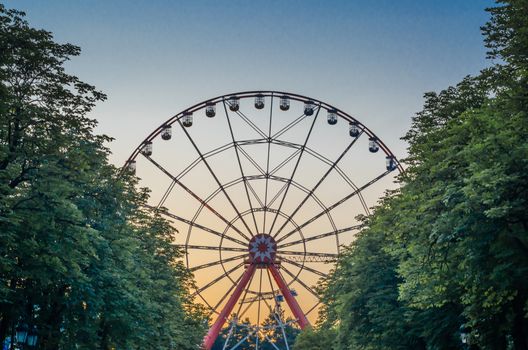part of ferris wheel in the park against the blue sky behind green trees