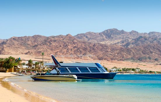 two boats at the surf on the background of the beach with palm trees and high rocky mountains in Egypt