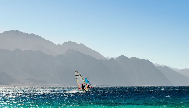 two windsurfers ride on the background of high rocky mountains in Egypt Dahab