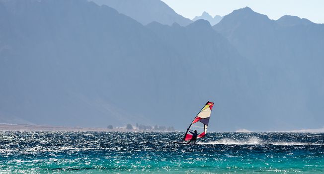 windsurfer rides in the Red Sea against the backdrop of high rocky mountains in Egypt Dahab