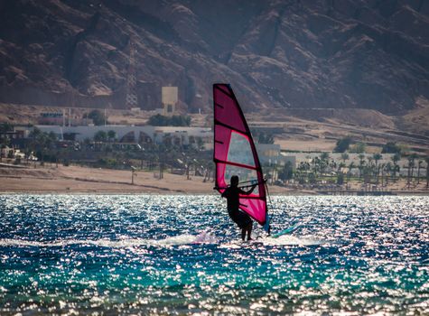 silhouette of a surfer in the Red Sea on the background of a rocky coast with palm trees and a hotel in Egypt