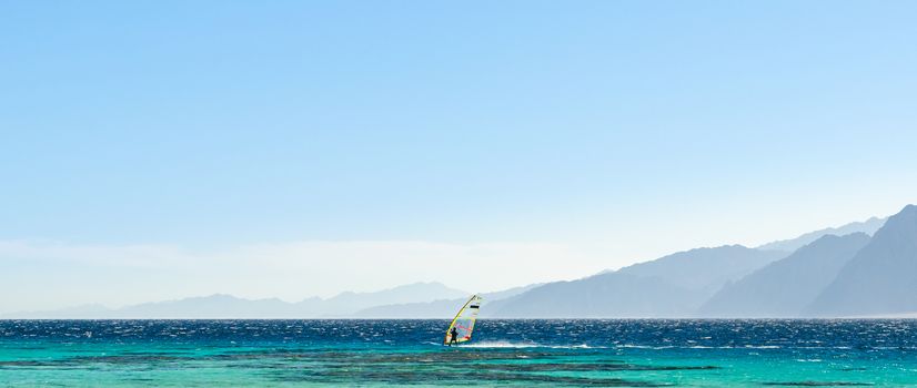 surfer rides in the Red Sea against the backdrop of high rocky mountains and a blue sky with clouds in Egypt Dahab