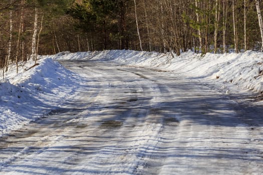 road covered with snow and ice in the forest on a sunny winter day