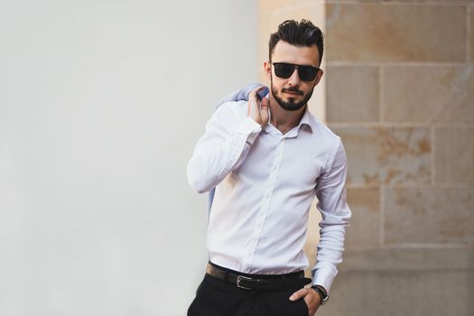 Portrait of elegant and fashionable man in black sunglasses posing on the street