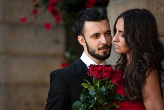 Portrait of an elegant fashion couple in love on a romantic date. Man giving a bouquet of red roses to a woman. 