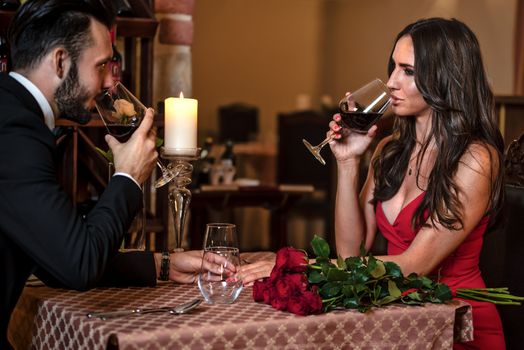 Couple in love holding hands and drinking wine during a romantic dinner at the restaurant.
