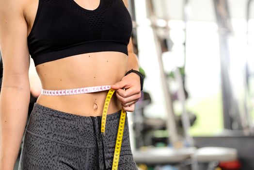 Healthy lifestyle concept - woman after workout at the gym measures her perfect waistline with a measuring tape in close-up