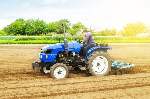 A white caucasian farmer on a tractor making ridges and mounds rows on a farm field. Preparing the land for planting future crop plants. Cultivation of soil for planting. Agroindustry, agribusiness.