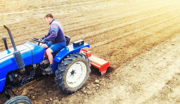 A farmer on a tractor cultivates a farm field. Field land preparation for new crop planting. Grinding and loosening soil, removing plants and roots from past harvest. Cultivation equipment.