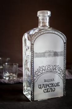 On a dark background, a beautiful large bottle of vodka Tsarskoye Selo and two glasses.