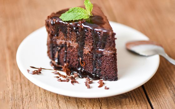 Cake chocolate sauce delicious dessert served on the table / cake slice on white plate with topping chocolate and mint leaf  