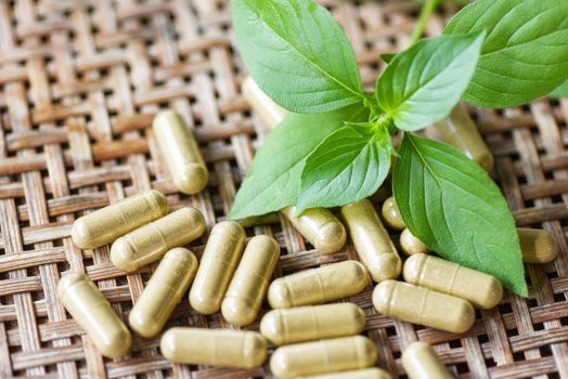 Herbal medicine extract from nature Non-toxic drug organic product on wooden scoop and green basil leaf / Herbal capsules from herbs healthy lifestyle