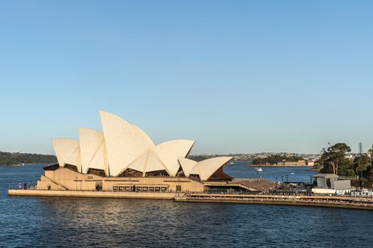 Sydney, Australia - February 12, 2019: Side view of the Opera House during sunset. Blue sky and water. Horizon is north shore of bay.
