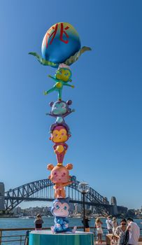 Sydney, Australia - February 11, 2019: Chinese New Year statue of five child-like figures, one on top of the other, on eastern boardwalk of Circular Bay. Harbour bridge in back, blue sky and people.