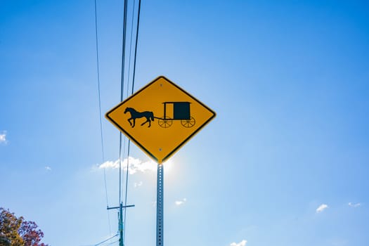 Sun shines from behind Amish traditional horse and buggy road sign in Lancaster County Pennsylvania, USA.