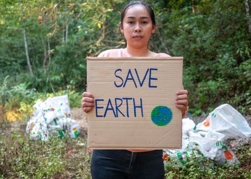 The young woman holding "Save The Earth" Poster showing a sign protesting against plastic pollution in the forest. The concept of World Environment Day. Zero waste.