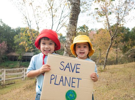 Two little child girl siblings holding "Save the planet" Poster showing a sign protesting against plastic pollution in the forest. The concept of World Environment Day. Zero waste.