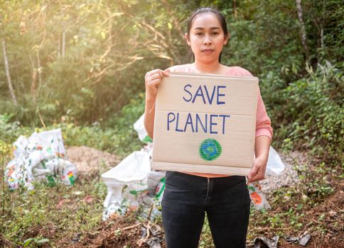 The young woman holding "Save the planet" Poster showing a sign protesting against plastic pollution in the forest. The concept of World Environment Day. Zero waste.