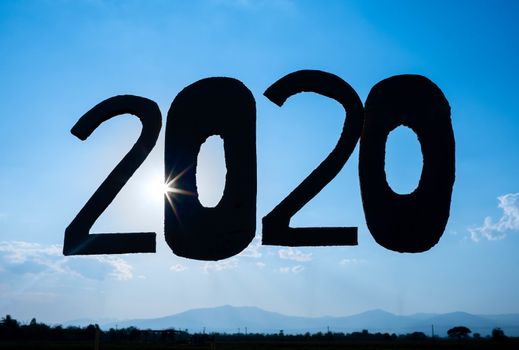 Recycle cardboard into 2020 numbers over blue sky background and the sun shining through the text. Concepts of New Year and celebration.
