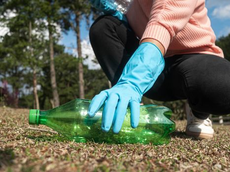 Close up hand of volunteer in gloves picks up a plastic bottle from the grass in the park. Concepts of save environment and stop plastic pollution.