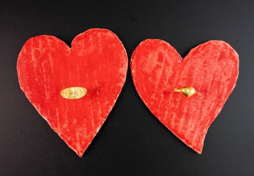 Two red heart-shaped recycled cardboard with wedding rings , isolated on dark background. Love symbol for valentines day. Concepts of Love and Romance.