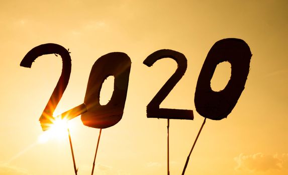 Silhouette of recycle cardboard into 2020 numbers over sunset sky background and the sun shining through the text. Concepts of New Year and celebration.