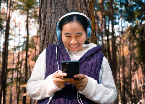 Asian young girl listening to music by headphone in the garden. Technology and relaxation concept.