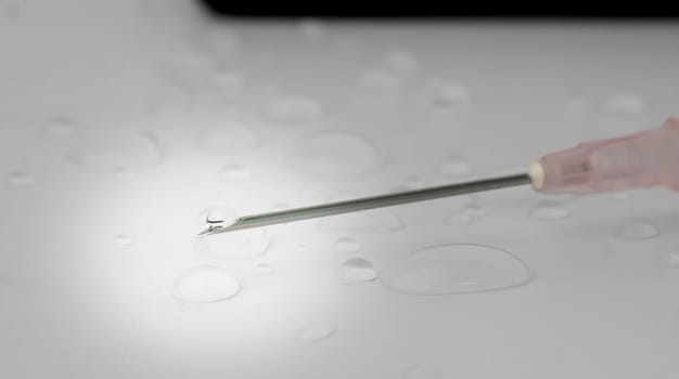 Drops of water with medical equipment syringe needle on white background. Selective focus.