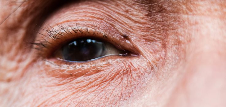 Close-up of one eye of an elderly Asian person with wrinkles around the eyes.