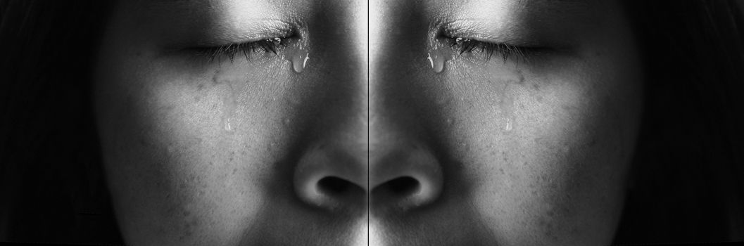 Close-up face of Asian woman crying with tears, isolated on dark background. Concepts of emotion and expression of human.