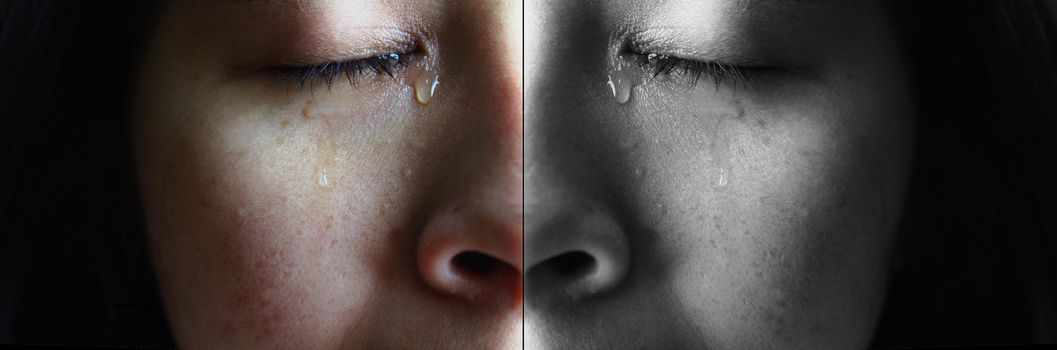 Close-up face of Asian woman crying with tears, isolated on dark background. Concepts of emotion and expression of human.