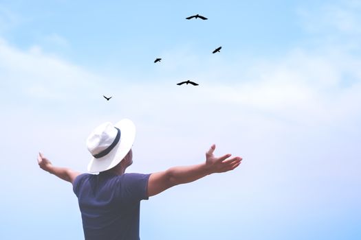 Man rise hands up to sky looking at birds fly through metaphor freedom concept with sunset sky and summer beach background.