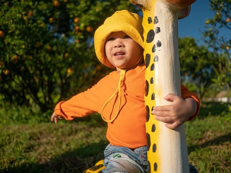 Adorable child girl enjoy sitting on giraffe statue 's back in the orange garden. Children do outdoor activities with family on holidays.