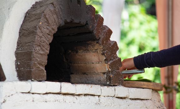 Asian woman baking homemade pizza in traditional clay oven at home.