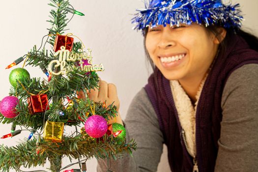 Woman wearing New Year's party hat decorating Christmas tree with baubles, lights and small gift presents for new year isolated on white background.