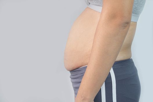 Close-up side view of woman excessive belly fat isolated on gray background. Woman fat belly. Obesity and Overweight Concept.