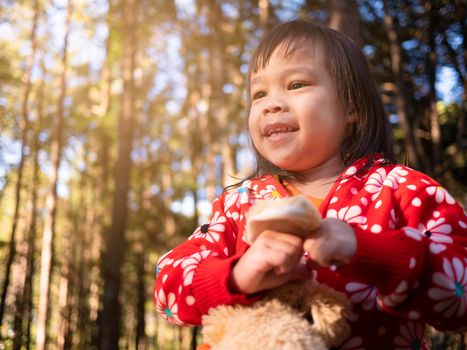 Happy Asian little child girl gone camping at pine forest with family on winter seasons. The concept of outdoor activities and adventures in nature for kids.