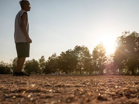 Asian senior man jogging in the park over sunset sky background. Healthy lifestyle and Healthcare concept.