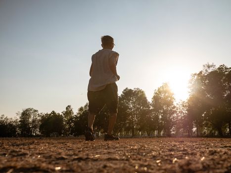 Asian senior man jogging in the park over sunset sky background. Healthy lifestyle and Healthcare concept.