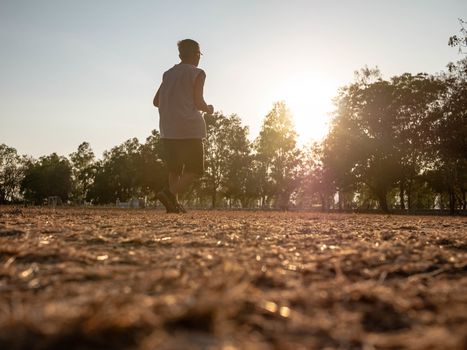 Asian senior man jogging in the park over sunset sky background. Healthy lifestyle and Healthcare concept.