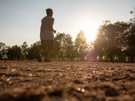 Asian senior man jogging in the park over sunset sky background. Healthy lifestyle and Healthcare concept.