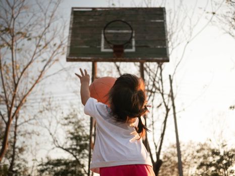 Cute little Asian child playing basketball on playground on summer day. Healthy outdoor sport for young child.